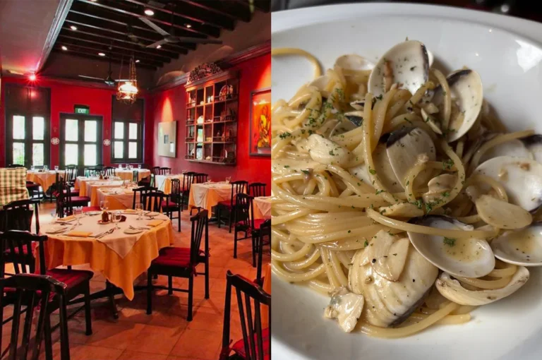A cozy, classic Italian restaurant with red walls and white tablecloths, featuring a plate of spaghetti alle vongole with fresh clams and garlic.
