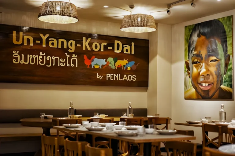 Cozy restaurant interior with wooden decor and tables set for dining. A large sign reads "Un-Yang-Kor-Dai" above colorful animal illustrations. A vibrant portrait of a smiling child is on the wall, creating a welcoming and warm atmosphere.