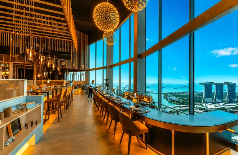 Elegant romantic rooftop dining Singapore experience inside a sophisticated restaurant in Singapore with floor‑to‑ceiling windows revealing stunning views of Marina Bay, Marina Bay Sands, the Singapore skyline, and skyline views at sea level. Perfect for a romantic date night, corporate events, or celebrations, this fine dining destination ranks among the most romantic restaurants and rooftop restaurants, offering contemporary Asian cuisine and Italian restaurant classics. Guests enjoy great food, steaks, wine, signature cocktails, and an imaginative menu by an executive chef, paired with impeccable service, a la carte dishes, and a new menu. The city skyline, city lights, and breathtaking views create an evening backdrop ideal for lunch, dinner, afternoon bites, or night occasions. Located near Collyer Quay, the rooftop bar and dining space invite guests to sip drinks, explore flavours, and feast on quality dishes in an elegant yet casual atmosphere. Surrounded by world‑class restaurants and bars, friends and couples soak in the sunset, taste every bite, and delight in a blend of fun and romance. This location offers access to the east, tickets to exclusive events, and a chance to literally miss nothing while enjoying food, cocktails, and meals that turn any date into a memorable occasion.