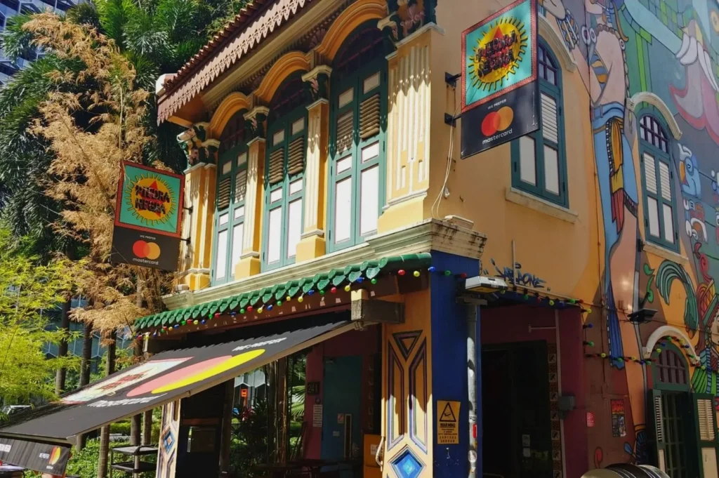 Colorful two-story building with ornate windows and vibrant murals. Signs with colorful logos hang outside. Bright, lively atmosphere.