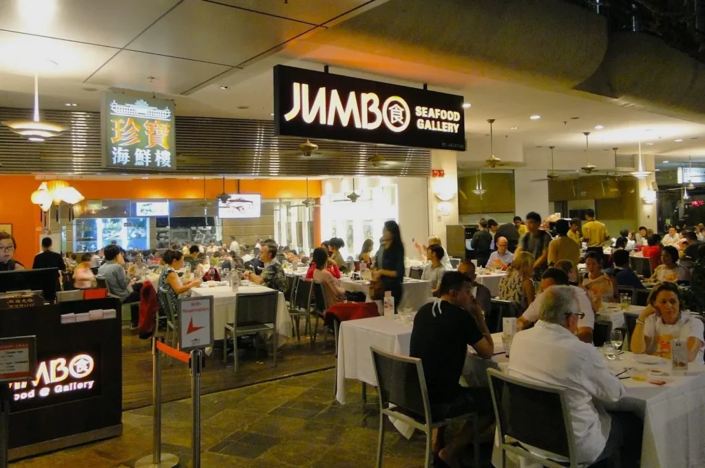 A bustling seafood restaurant, "Jumbo Seafood Gallery," with diners enjoying meals at white tablecloth tables, conveys a vibrant and lively atmosphere.