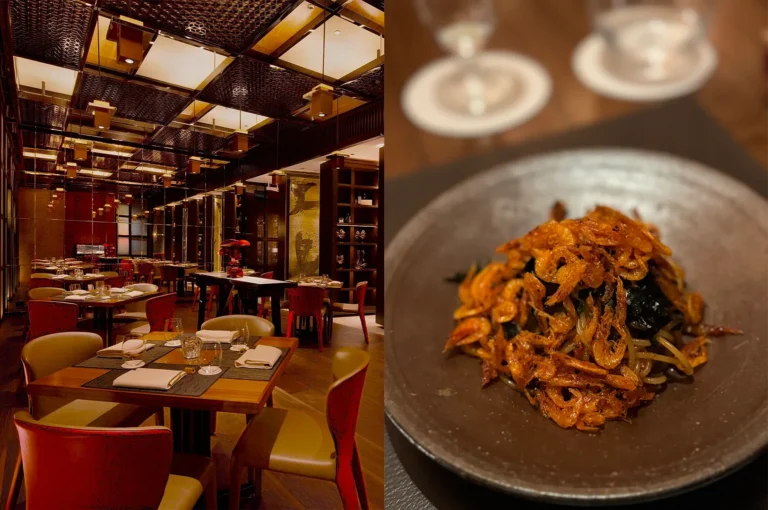 The interior of a high-end Chinese restaurant with ornate gold ceiling panels and a dish of noodles topped with crispy fried shrimp.