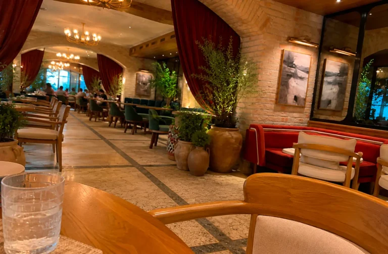 Elegant restaurant interior with burgundy drapes, chandeliers, terracotta planters, and wooden furniture with cream cushions