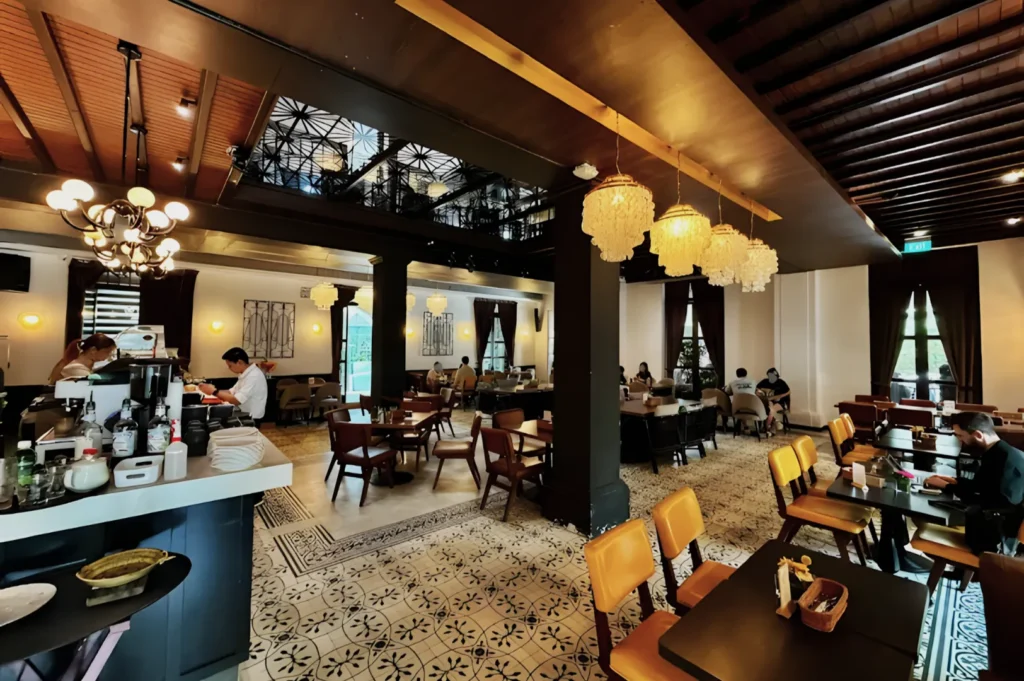 Stylish cafe interior with patterned tile floor and warm lighting. Wooden furniture fills the space, people seated at tables. Cozy, inviting atmosphere.