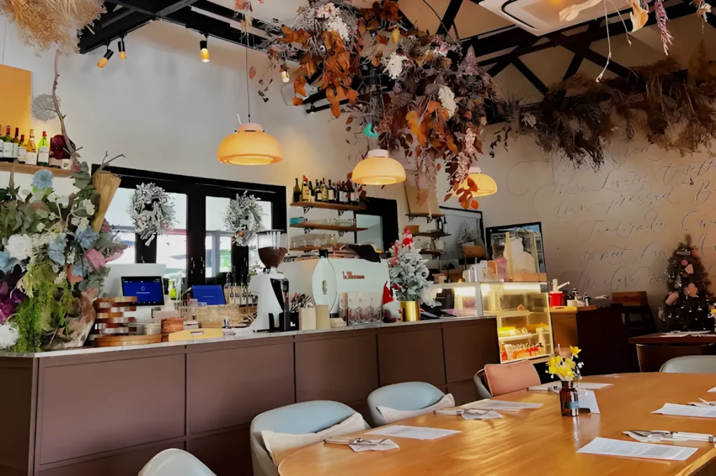 Cozy café interior with warm lighting, dried floral decorations, and rustic décor. A wooden table is set for dining, with chic ceiling fixtures.