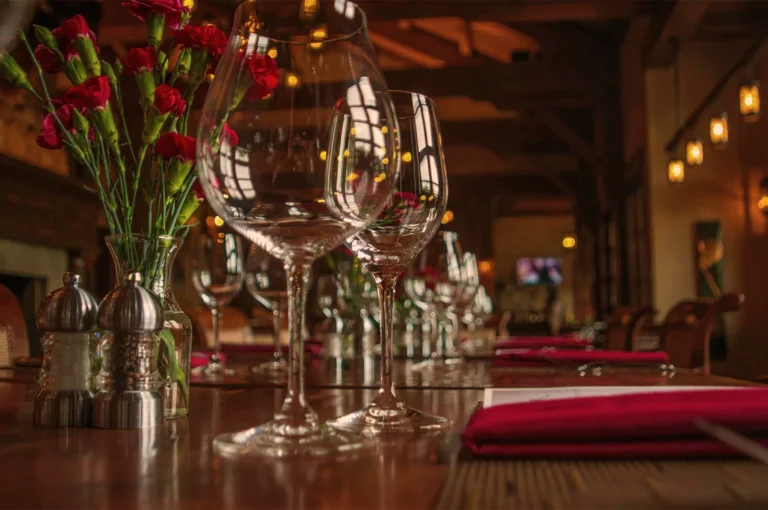 Elegant restaurant interior with red flowers in a vase and empty wine glasses on a wooden table. Warm lighting creates an inviting atmosphere.