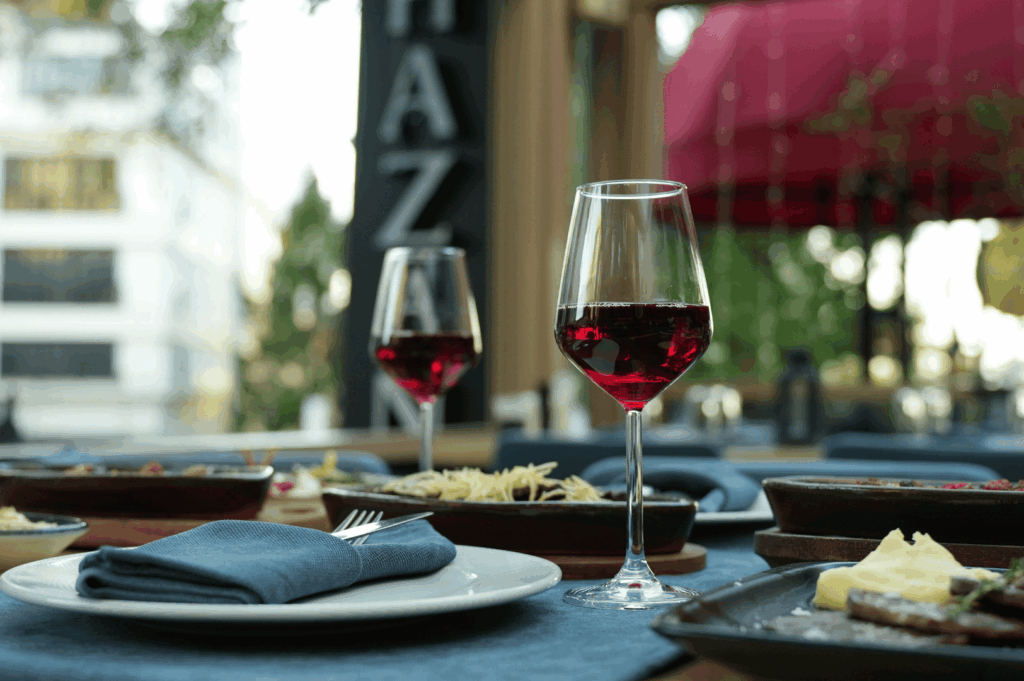 Open-air dining table with blue linens, red wine, and a spread of pasta and cheese dishes—capturing the relaxed elegance and convivial spirit of a private meal under a canopy of greenery.