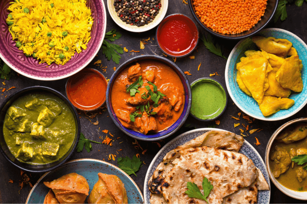 Vibrant spread of authentic Indian cuisine featuring turmeric rice, red and green curries, paneer, samosas, naan, and colorful chutneys, artfully arranged on a dark surface—showcasing the rich flavors and culinary diversity found in Little India, Singapore.