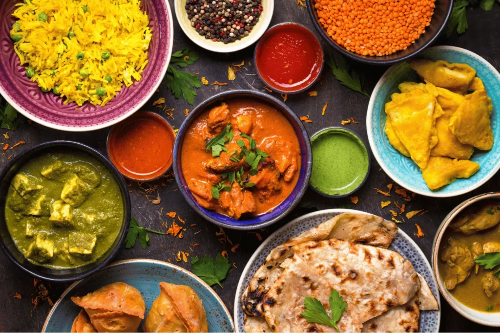 Vibrant spread of authentic Indian cuisine featuring turmeric rice, red and green curries, paneer, samosas, naan, and colorful chutneys, artfully arranged on a dark surface—showcasing the rich flavors and culinary diversity found in Little India, Singapore.