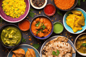 Vibrant spread of authentic Indian cuisine featuring turmeric rice, red and green curries, paneer, samosas, naan, and colorful chutneys, artfully arranged on a dark surface—showcasing the rich flavors and culinary diversity found in Little India, Singapore.