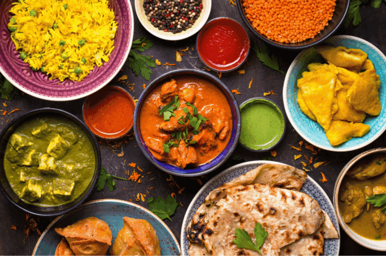 Vibrant spread of authentic Indian cuisine featuring turmeric rice, red and green curries, paneer, samosas, naan, and colorful chutneys, artfully arranged on a dark surface—showcasing the rich flavors and culinary diversity found in Little India, Singapore.