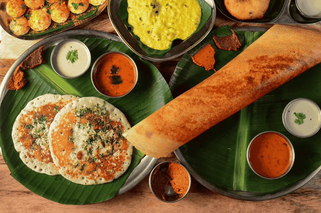 Traditional South Indian breakfast served on banana leaves and metal plates, featuring uttapams, crispy dosa, assorted chutneys, sambar, lentil curry, and paniyarams—celebrating the vibrant flavors and cultural authenticity of Little India, Singapore.