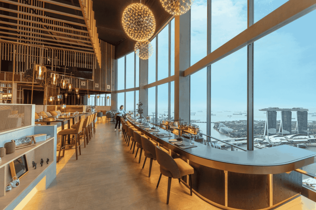 Elegant romantic rooftop dining Singapore experience inside a sophisticated restaurant in Singapore with floor‑to‑ceiling windows revealing stunning views of Marina Bay, Marina Bay Sands, the Singapore skyline, and skyline views at sea level. Perfect for a romantic date night, corporate events, or celebrations, this fine dining destination ranks among the most romantic restaurants and rooftop restaurants, offering contemporary Asian cuisine and Italian restaurant classics. Guests enjoy great food, steaks, wine, signature cocktails, and an imaginative menu by an executive chef, paired with impeccable service, a la carte dishes, and a new menu. The city skyline, city lights, and breathtaking views create an evening backdrop ideal for lunch, dinner, afternoon bites, or night occasions. Located near Collyer Quay, the rooftop bar and dining space invite guests to sip drinks, explore flavours, and feast on quality dishes in an elegant yet casual atmosphere. Surrounded by world‑class restaurants and bars, friends and couples soak in the sunset, taste every bite, and delight in a blend of fun and romance. This location offers access to the east, tickets to exclusive events, and a chance to literally miss nothing while enjoying food, cocktails, and meals that turn any date into a memorable occasion.