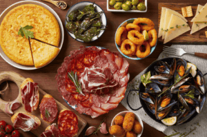 A vibrant spread of Spanish cuisine showcasing Spanish food and traditional Spanish dishes, featuring a Spanish omelette, patatas bravas with tomato sauce, pimientos de padrón (de padrón), cured ham, chorizo, black pudding, and blood sausage, alongside fresh bread and crusty bread drizzled with olive oil. This famous Spanish dish selection reflects traditional Spanish recipes and Spanish classics, from seafood paella and other rice dishes to rabo de toro (braised oxtail) and mojo picón from the Canary Islands and Canarian cuisine. Highlights include popular tapa plates, deep fried croquettes with bechamel sauce, green peppers, garlic, and other ingredients served for a dinner party with loved ones. Inspired by Basque Country, La Rioja, and the Iberian Peninsula, these traditional dishes—from national dish paella to ultimate Spanish comfort food—are served hot with meat, chicken, pork fat, ground beef, seafood, and white rice. Perfect for those who visit Spain, dine at a restaurant like El Celler de Can Roca (El Celler), or are a huge fan of Spanish cooking. This delicious meal captures the rich flavor of Spain, its cuisine, and popular dishes, paired with popular desserts like dessert chocolate creations and dairy products. A feast to eat, taste, and celebrate food culture.