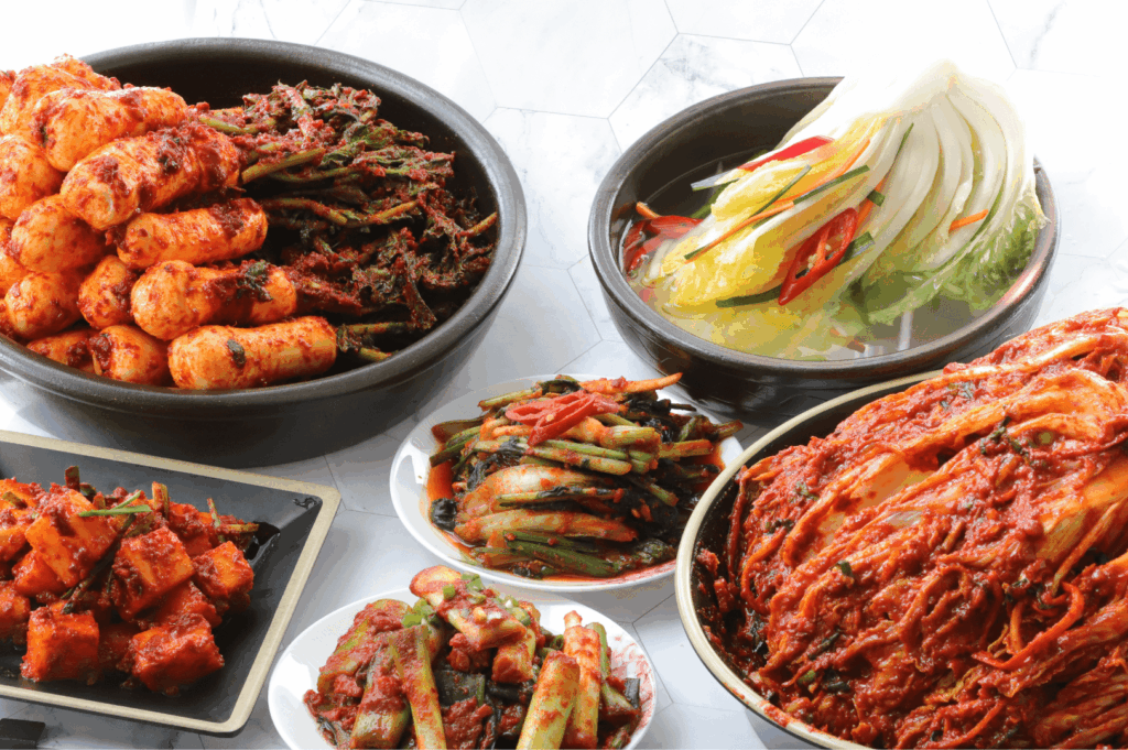 Assorted traditional Korean kimchi dishes including napa cabbage kimchi, radish kimchi, cucumber kimchi, and water kimchi, beautifully presented as part of a comforting Korean cuisine spread at a Korean BBQ restaurant in Singapore. Perfect for sharing platters, side dishes, and la carte menu options at top Korean restaurants like Charim Korean BBQ, Wang Dae Bak, and Hanjip Korean Grill House. Ideal for pairing with grilled meats, pork belly, USDA prime beef, beef brisket, Mul Gogi Korean BBQ and Korean fried chicken, this vibrant display highlights the rich flavors of Korean cooking and authentic Korean food culture.