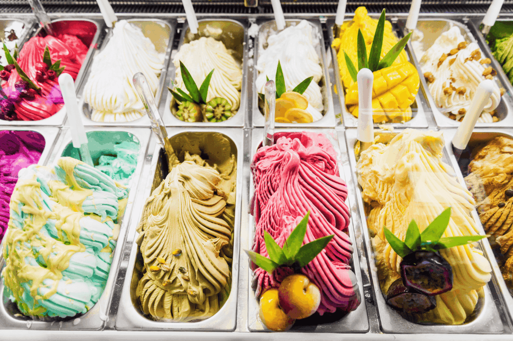 Colorful display of artisanal gelato in an Italian restaurant, part of authentic Italian cuisine and Italian food culture, presented with expert food styling to highlight iconic Italian dishes and indulgent desserts from northern Italy to southern Italy. The gelato, made with buffalo milk, milk, sugar, and wheat flour-based cones or bread accompaniments, is typically served alongside great food such as fresh pasta, stuffed pasta, pizza, risotto, and baked main courses. Various sauces like tomato sauce, meat sauce, pesto sauce, olive oil, extra virgin olive oil, balsamic vinegar, lemon juice, melted butter, and parmesan cheese complement traditional dishes that vary depending on the region, from Emilia Romagna specialties to seafood, chicken, beef, and prosciutto recipes. Fresh vegetables, ripe tomatoes, potatoes, cannellini beans, pine nuts, herbs, oregano, and garlic are primary ingredients in many variations of pasta varieties, dough-based meals, and desserts served in Italy. This presentation reflects a deep connection to the long history of Italian cooking, where meat, sauce, cheese, and pasta dishes are cooked with butter, salt, and lemon for balanced flavor, creating great food experiences that celebrate Italy’s culinary heritage.
