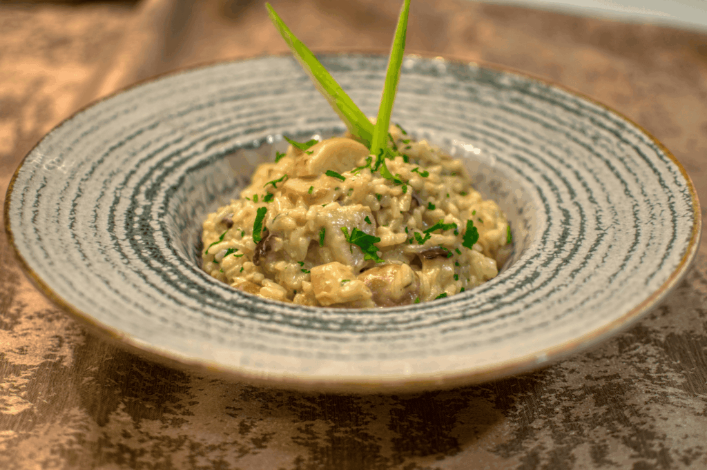 Authentic Italian cuisine risotto, a traditional dish from northern Italy and southern Italy, beautifully presented with expert food styling in an Italian restaurant, showcasing Italian food and iconic dishes made with olive oil, extra virgin olive oil, fresh vegetables, herbs, garlic, potatoes, ripe tomatoes, and parmesan cheese. This Italian dish, inspired by the long history of Italy’s pasta varieties and main courses, is typically served alongside fresh pasta, stuffed pasta, baked meals, pizza, bread, and indulgent desserts. The creamy risotto features mozzarella cheese, buffalo milk, melted butter, milk, salt, lemon juice, lemon zest, and a deep connection to Emilia Romagna recipes, with many variations that vary depending on the primary ingredient—whether meat sauce, pesto sauce, tomato sauce, meat, beef, chicken, seafood, prosciutto, or vegetables. Enhanced with balsamic vinegar, pine nuts, cannellini beans, oregano, dough, and wheat flour, this great food reflects various sauces and pasta traditions, from pesto to meat sauce, and is cooked to perfection. Served as part of Italian main courses and desserts, this meal celebrates Italian culture, cheese, sauce, and food heritage, making it one of Italy’s most beloved dishes.