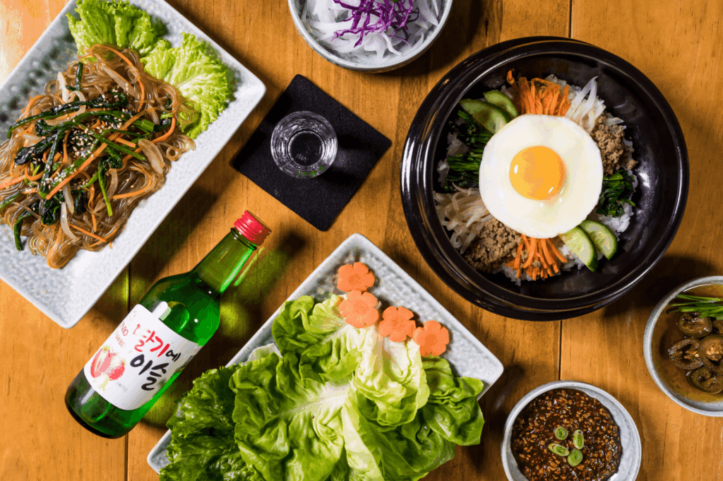 A vibrant spread of Korean cuisine in Singapore at a cozy Korean restaurant, featuring colorful k bbq la carte dishes such as bibimbap, japchae, fresh lettuce wraps, assorted side dishes, and banchan. Perfect for sharing dishes and comforting Korean dishes, this table showcases the essence of Korean food and Korean cooking with options found in popular Korean restaurants in Singapore like Charim Korean BBQ, Wang Dae Bak, and Hanjip Korean Grill House. Ideal for special occasions or casual dining, the menu could include pork belly, USDA prime beef, beef brisket, marinated chicken, seafood pancake, kimchi stew, kimchi fried rice, steamed dumplings, chewy rice cakes in spicy tteokbokki sauce, and premium meat cuts from Korean BBQ and Korean charcoal BBQ spots. A feast that excites the taste buds, blending comfort food with premium cuts and grilled meats from bbq sets, ala carte items, and set menus at the best Korean dining destinations in Clarke Quay, Jalan Jurong Kechil, or Rochester Chingu