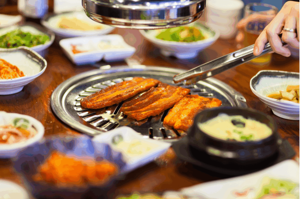 Korean barbecue meal in progress at a korean bbq restaurant featuring pork belly and pork set grilled on the main grill, surrounded by comforting korean dishes like kimchi stew, steamed dumplings, rice cakes, and side dishes. This korean cuisine experience showcases grilled meats, premium meat cuts including beef brisket, beef short rib, pork jowl, pork collar, marinated chicken, kurobuta berkshire pork, and usda prime beef. Diners enjoy ala carte items, sharing platter, and set menus with attentive service in private dining rooms—perfect for special occasions and taste buds craving korean food. Popular at korean restaurants in singapore such as charim korean bbq, wang dae bak, hanjip korean grill house, mul gogi korean bbq, don dae bak, dae bak, woo dae galbi, pohang seafood, and seoul restaurant. Located near clarke quay and jalan jurong kechil, these kbbq restaurants offer la carte dishes, la carte options, la carte menu, lunch sets, bbq sets, buffet menu, and comfort food like fried rice, kimchi fried rice, black bean noodles, spicy tteokbokki sauce, chewy rice cakes, mozzarella cheese, korean fried chicken, fried chicken, seafood pancake, kimchi pancake, and free flow eggs. Discover the best korean bbq menu with premium cuts, korean charcoal bbq, korean charcoal, sharing dishes, and the four flavours from sister brand rochester chingu—celebrating authentic korean cooking and korean cuisine in singapore with every korean term and bite.