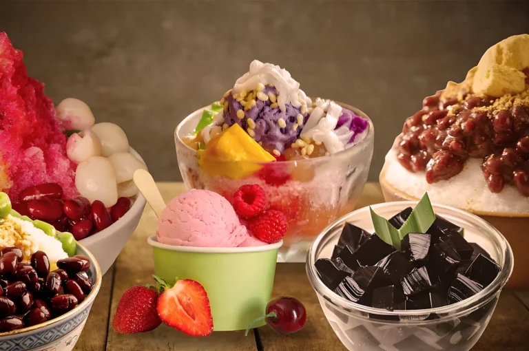 Five bowls of vibrant ice treats on a wooden table include shaved ice with fruits, red beans, colorful jellies, and a scoop of pink ice cream with berries.