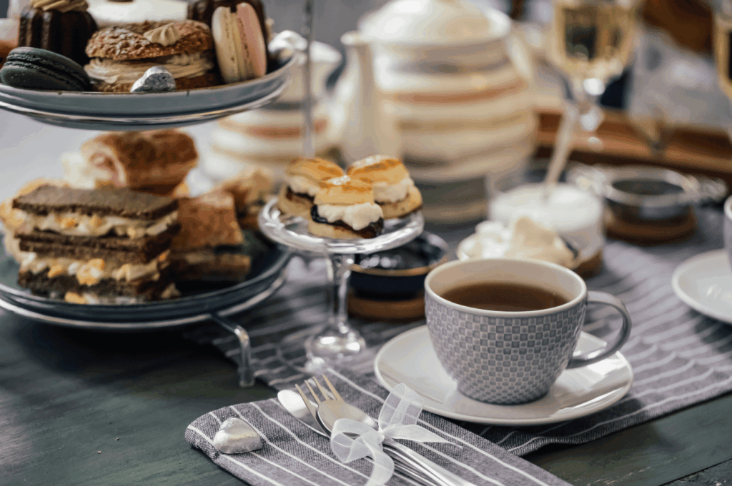 Elegant afternoon tea celebration with tiered trays of macarons, layered cakes, and cream-filled pastries, paired with champagne and floral teaware. A ribbon-tied napkin set and patterned cup add charm to the refined table setting—capturing Singapore’s fusion of luxury, artistry, and social dining tradition.