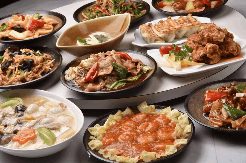 A colorful array of Chinese and pan-Asian dishes arranged on a Lazy Susan, capturing the communal spirit of regional dining traditions beyond Cantonese norms. Stir-fried vegetables, dumplings, fried chicken, soups, and meat entrees—featuring bell peppers, mushrooms, and green beans—create a vibrant, multi-textured feast. The rotating table emphasizes shared hospitality and the diversity of flavors found in Singapore’s evolving Chinese culinary landscape, from Hakka and Hunan to Teochew and Fujian influences.