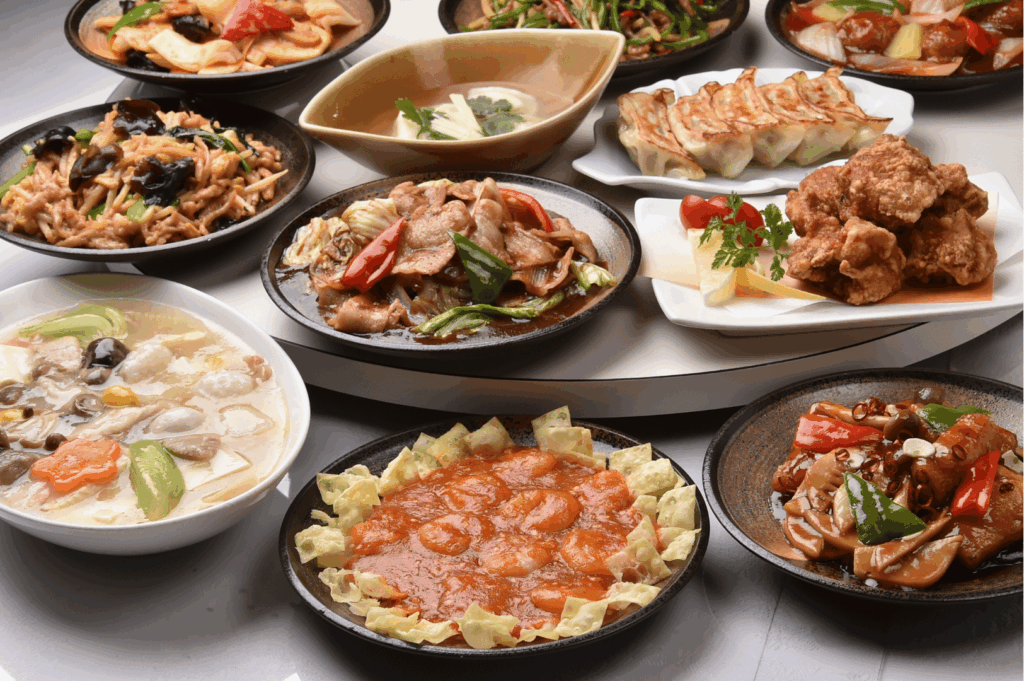 A vibrant tabletop spread of Chinese dishes, including stir-fried vegetables with meat, dumplings, fried chicken, seafood soup, and shrimp in red sauce surrounded by folded wonton wrappers. Each dish is plated separately, showcasing a kaleidoscope of textures and colors—from glossy sauces to crisp wrappers. The composition evokes festive abundance and culinary diversity, reflecting the layered influences of Hunan, Sichuan, and Teochew cuisines in Singapore’s Chinese food scene beyond Cantonese staples.