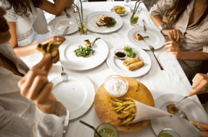 Friends sharing a vibrant spread of grilled vegetables, spring rolls, and fried green beans at a lively Singapore restaurant, with green iced drinks on the table — capturing the communal spirit of the city’s best group dining spots.