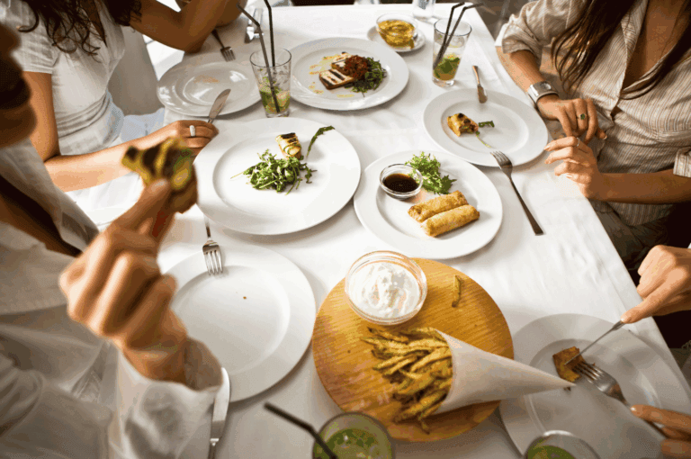 Friends sharing a vibrant spread of grilled vegetables, spring rolls, and fried green beans at a lively Singapore restaurant, with green iced drinks on the table — capturing the communal spirit of the city’s best group dining spots.