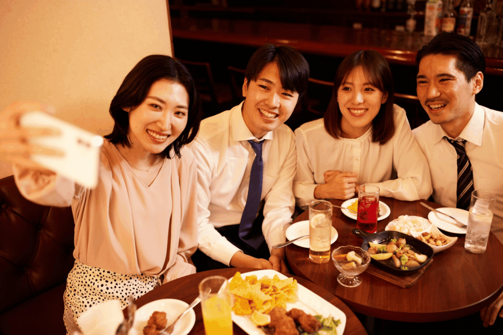 Group of friends smiling for a selfie over a table of fried chicken, nachos, and cocktails in a cozy Singapore restaurant — highlighting the fun, social side of group dining.