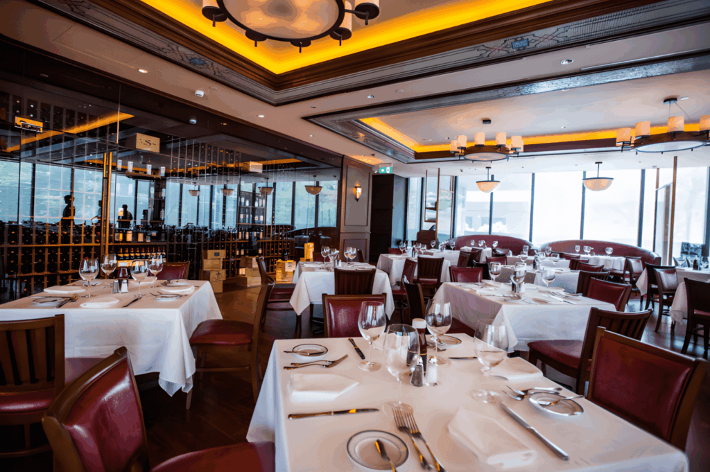 Elegant Singapore fine dining restaurant with white tablecloths, red leather chairs, chandeliers, and a mirrored wine wall — offering a refined group dining experience in a luxurious setting.