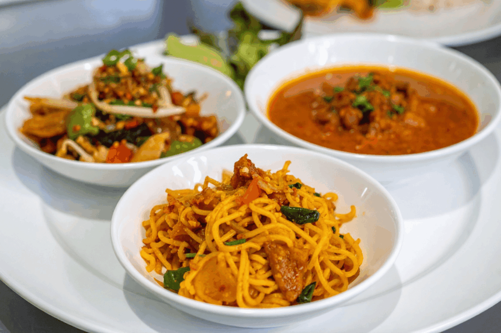 Three bowls of vibrant Peranakan dishes on a white plate, showcasing colorful heritage cuisine in Singapore.