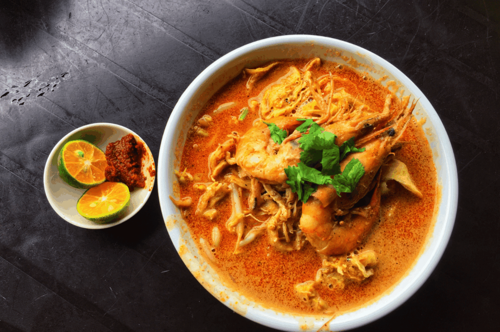 Bowl of Peranakan-style curry with shrimp and herbs on a dark tabletop, highlighting rich, aromatic gravy.