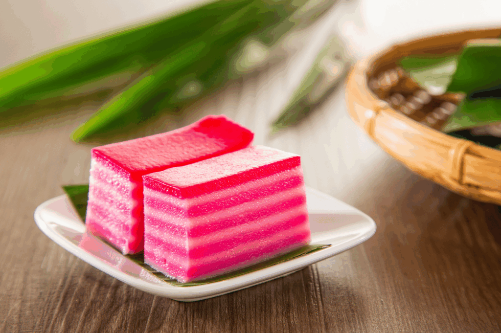 Two pieces of pink kueh lapis sagu (Peranakan layered jelly cake) on a white plate, highlighting the vibrant colors and delicate texture—Peranakan Cuisine in Singapore.
