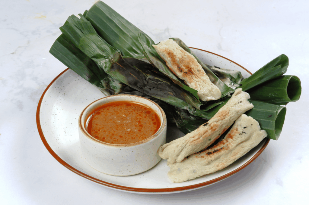 Close-up of a traditional serving on banana leaves with side dipping sauce, reflecting the vibrant flavors and presentation of Peranakan cuisine in Singapore.