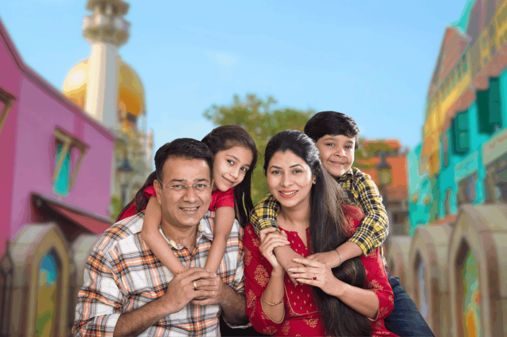 A joyful South Asian family of four poses together in front of a vibrant, color-splashed backdrop at a Singapore cultural district, evoking the warmth and diversity of regional Indian food traditions. The adults smile warmly while the children lean affectionately on their shoulders, framed by brightly painted buildings and a golden dome that hint at festive architecture. Their casual attire and relaxed expressions reflect the familial spirit and cross-generational connection central to Indian culinary heritage. Ideal for illustrating themes of cultural celebration, diaspora identity, and the communal joy of food in Singapore’s 2025 dining landscape.