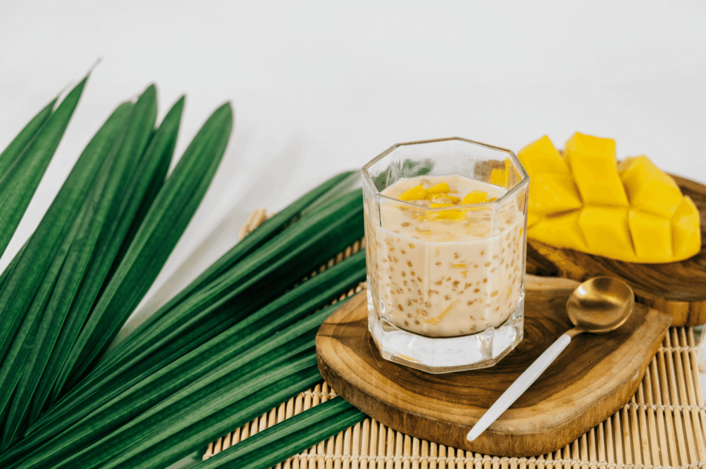 A glass of mango sago topped with fresh mango on a bamboo mat, styled for a feature on Singapore’s dessert culture.