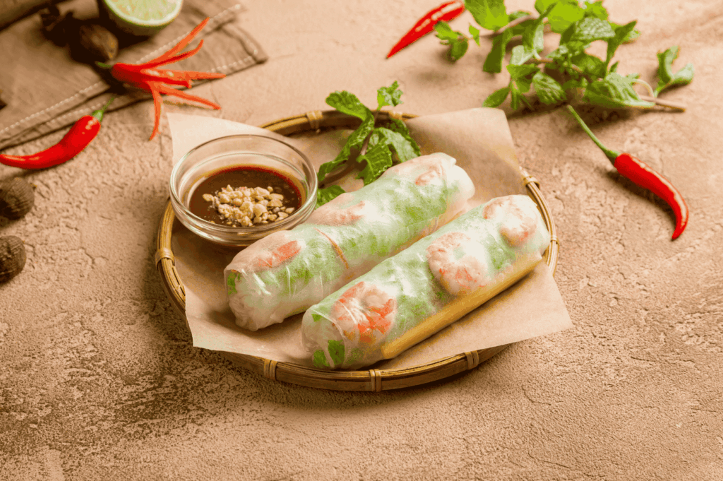 Fresh Vietnamese shrimp spring rolls on a bamboo tray in Singapore, filled with vermicelli noodles and herbs, served with peanut dipping sauce, mint leaves, and red chili for a vibrant street food presentation.