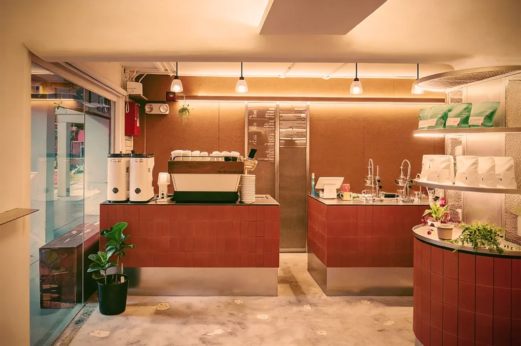 Modern minimalist coffee shop interior with warm lighting, red‑tiled counters, espresso machine, and cozy earthy tones.