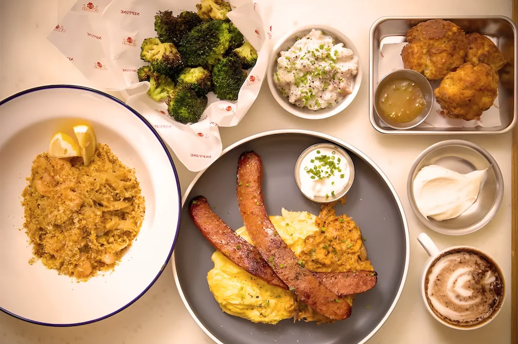 Delicious breakfast platter featuring sausages, mashed potatoes, roasted broccoli, pasta, biscuits, and creamy coffee.