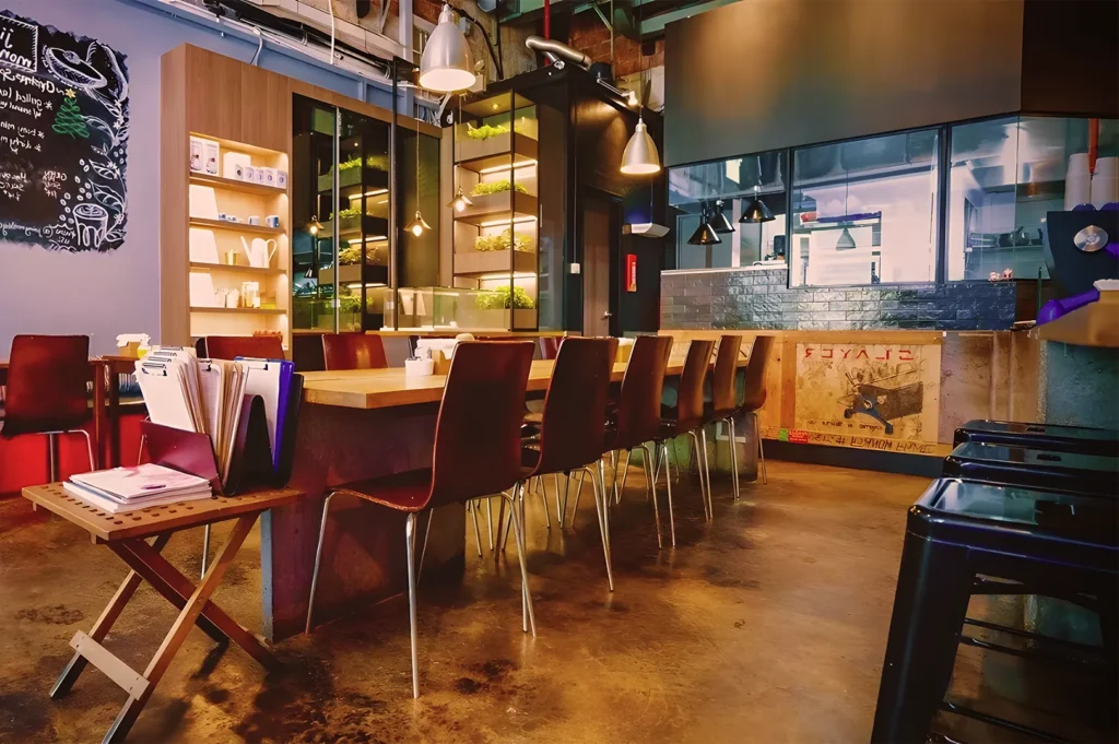 Trendy industrial café with wooden communal tables, pendant lights, chalkboard wall, and modern rustic décor.