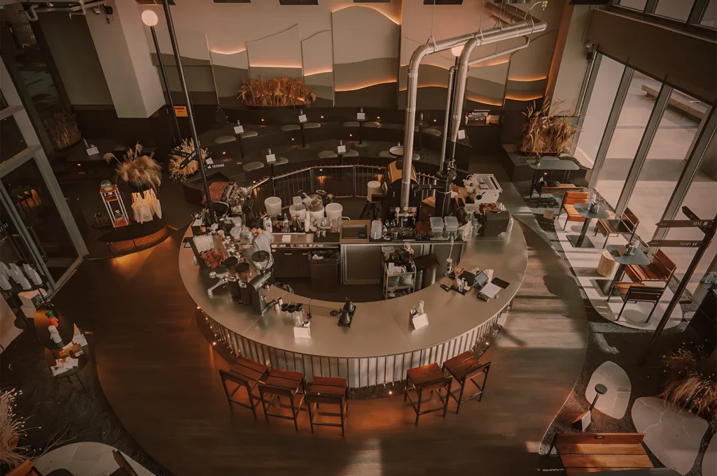 Contemporary café with circular coffee bar, espresso machines, wooden stools, and warm ambient lighting.