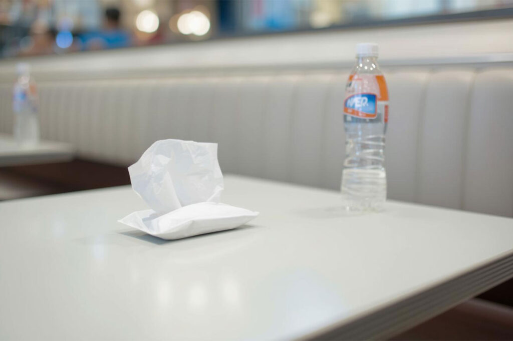 A single white packet of tissue paper placed on a clean, white table with a plastic water bottle, illustrating the Southeast Asian practice of "chope" (reserving a table).