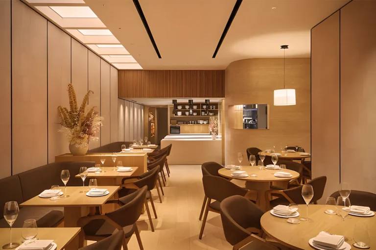 Elegant restaurant interior with round wooden tables, set for dining, surrounded by modern brown chairs. Soft lighting creates a warm, inviting ambiance.