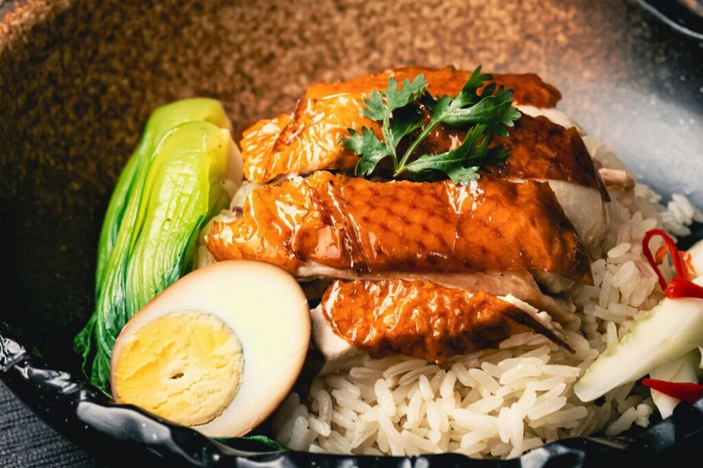 A bowl of rice topped with chicken, eggs, and vegetables, representing Singapore's diverse culinary identity.