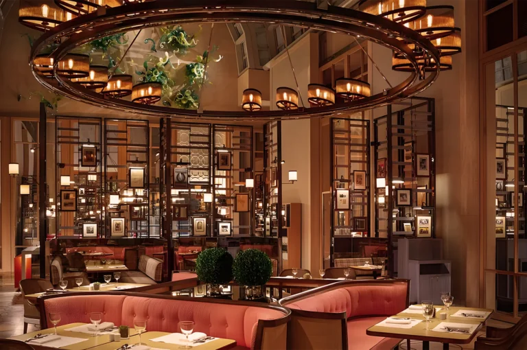 Luxurious fine‑dining restaurant interior with warm ambient lighting, plush pink booths, circular chandeliers, and framed art décor creating a sophisticated atmosphere.