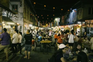 Bustling night market street with crowds dining at outdoor tables under string lanterns