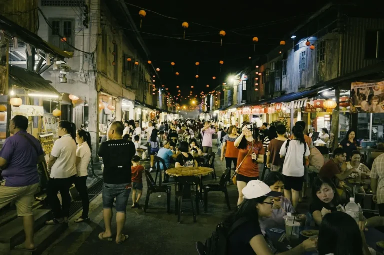 Bustling night market street with crowds dining at outdoor tables under string lanterns