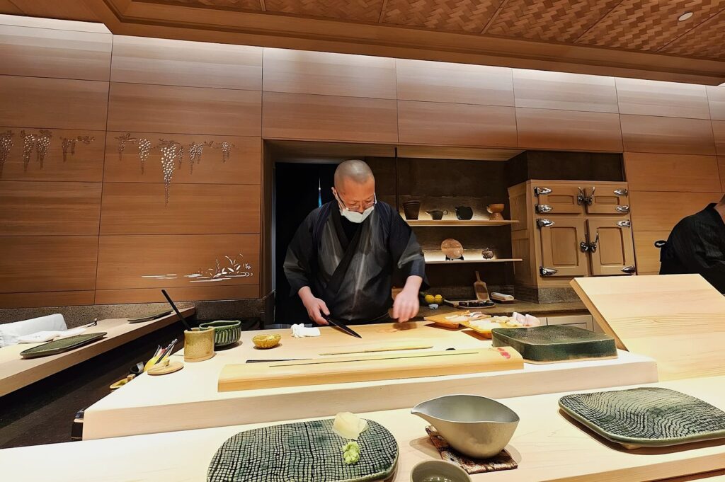 In the kitchen of Ginza Sushi Ichi, a man in a black shirt is preparing sushi.