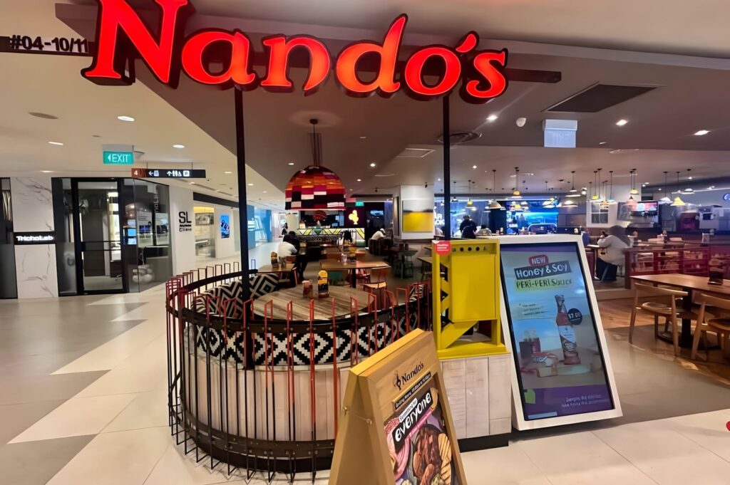 A bustling indoor shopping mall, Plaza Singapura, filled with shoppers walking and browsing various restaurants.